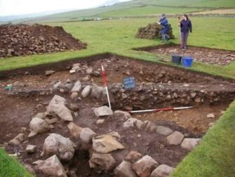 Archeologische opgraving in een grasveld met meetstokken en stenen