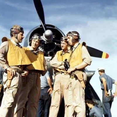 Vier bemanningsleden in uniform bij een historisch vliegtuig