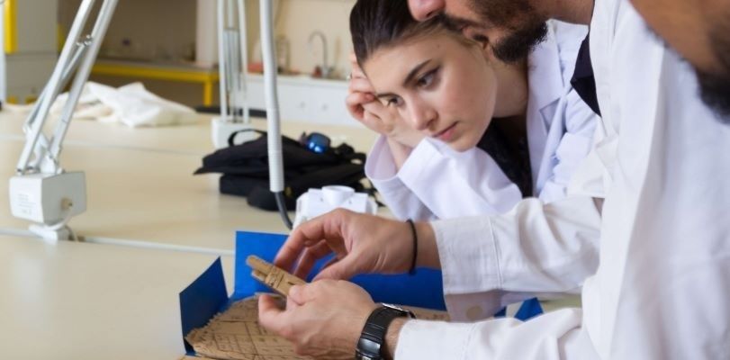 Onderzoekers in witte jassen onderzoeken een klein metalen onderdeel in een laboratorium